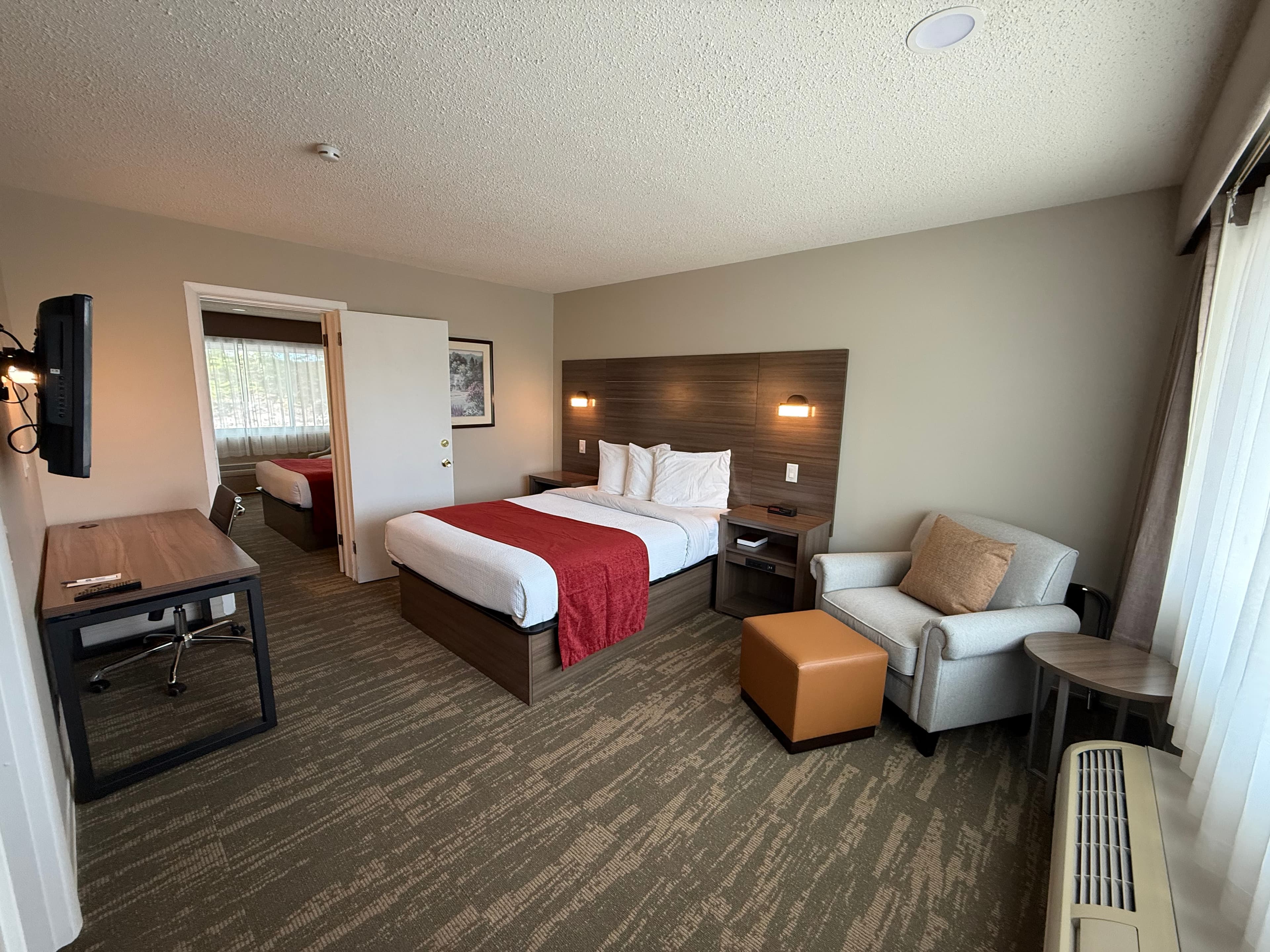 Spacious hotel suite with two king bedrooms, each featuring a desk, a cozy armchair, and a flat-screen TV