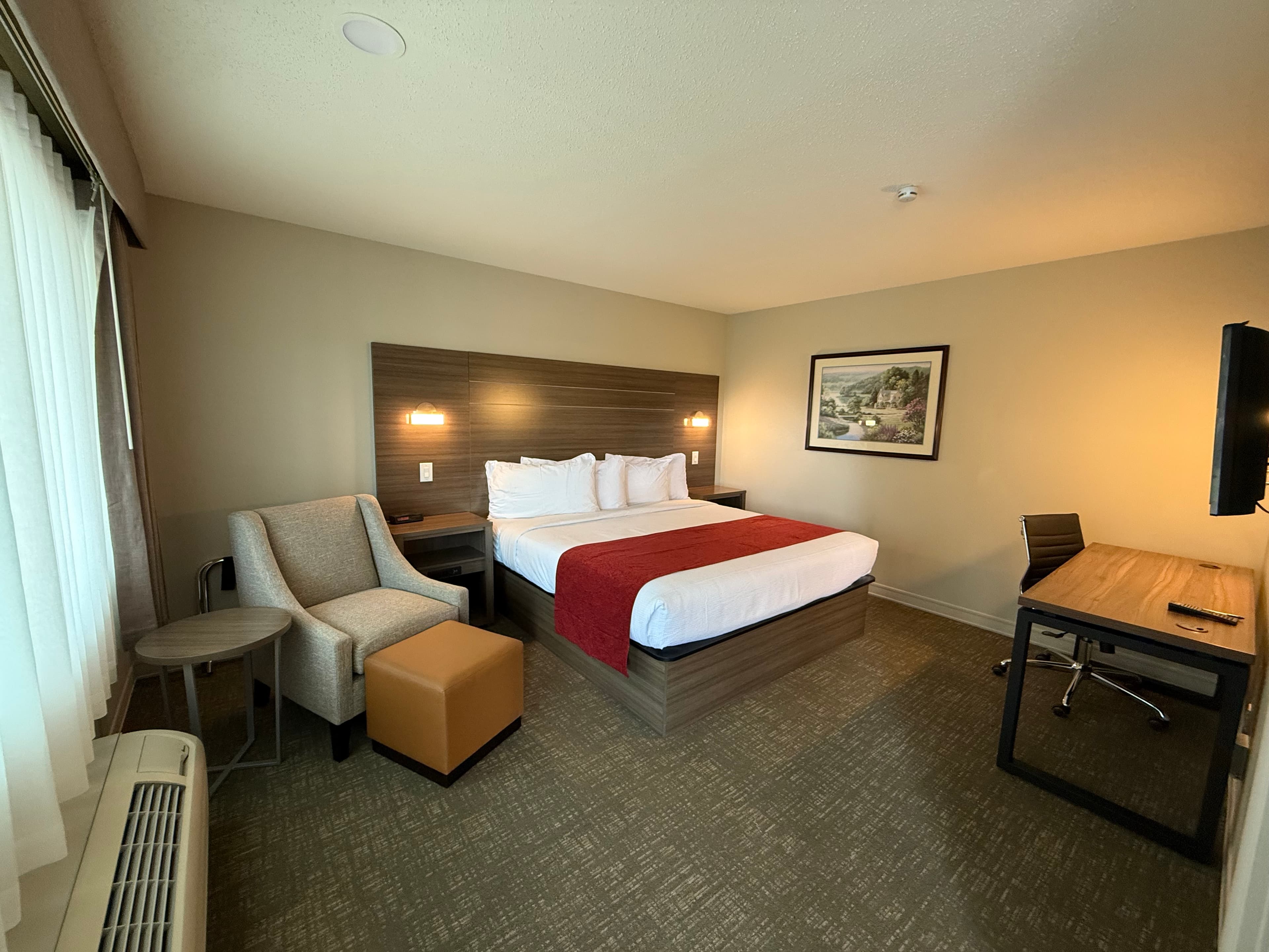 A spacious and modern hotel room with a king-size bed, a comfortable armchair with an ottoman, a desk with a chair, and a flat-screen TV.